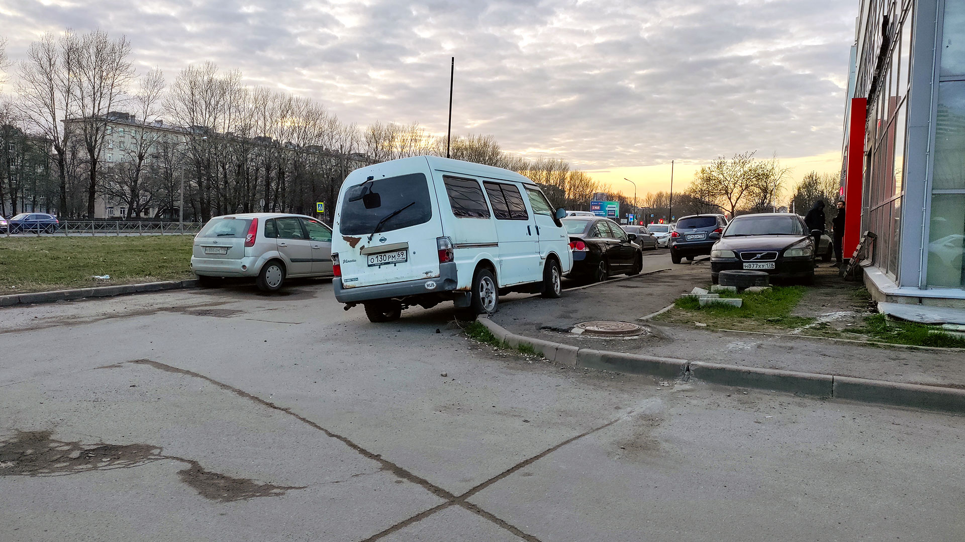 Какой штраф за езду по тротуару на машине? Автомобили припаркованы у тротуара возле здания, городская улица вечером